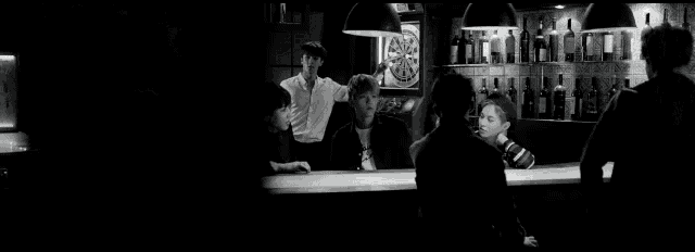 a black and white photo of a bar with a neon sign that says beer and drink .