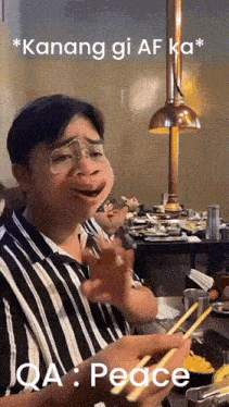 a man with glasses is sitting at a table with chopsticks and a caption saying peace