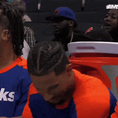 a man with a braided hairdo is sitting in a stadium watching a game