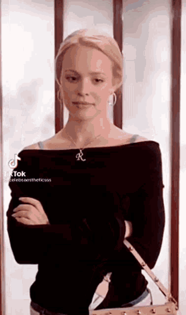 a woman in a black off the shoulder sweater is standing with her arms crossed and holding a purse .