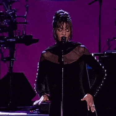 a woman in a black dress is singing into a microphone on stage