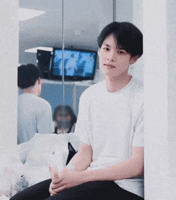 a young man in a white shirt is sitting in front of a mirror