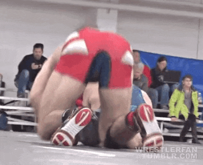 two men are wrestling on a wrestling mat in front of a crowd of people .