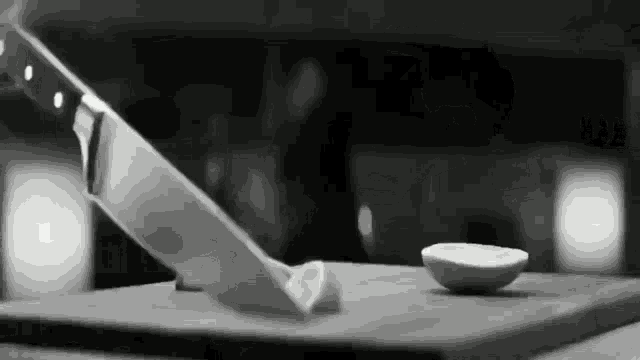 a black and white photo of a knife cutting a piece of lemon on a cutting board