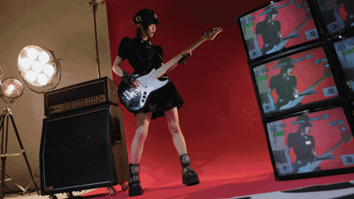 a woman playing a guitar in front of a stack of monitors that say ' rock ' on the screen