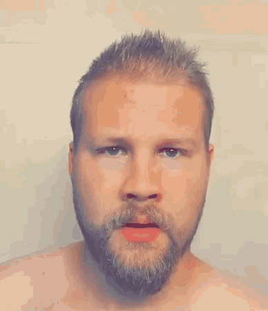 a shirtless man with a beard is looking at the camera with his mouth open