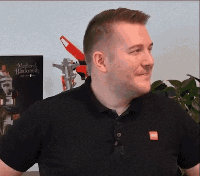 a man wearing a black polo shirt with a red lego logo on the sleeve is standing in front of a poster .