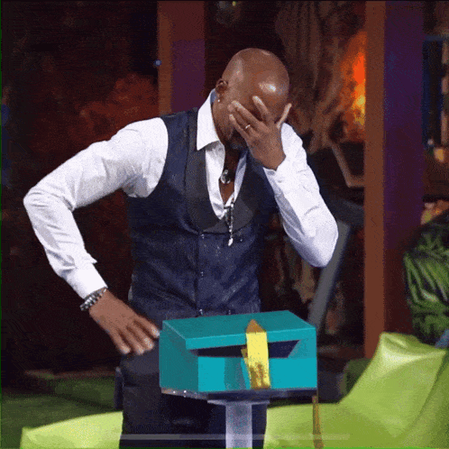 a man covering his face with his hand while standing next to a green box