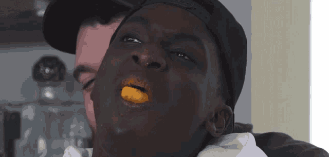 a man in a black hat is eating a slice of orange