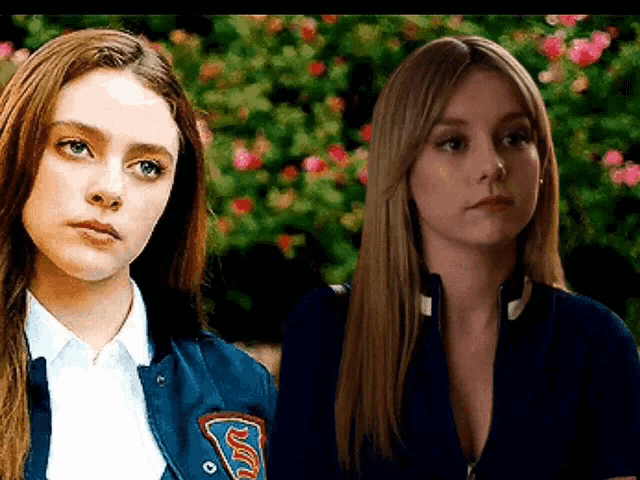 two women are standing next to each other and one of them is wearing a blue jacket with a patch on it .