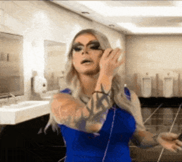 a woman in a blue dress is standing in a public restroom talking on a cell phone