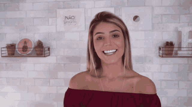 a woman in a red off the shoulder top smiles in front of a wall with a sign that says " não permite "