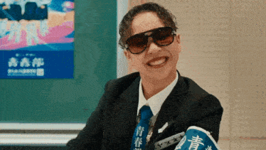 a man in a suit and tie is smiling in front of a blackboard with chinese writing on it