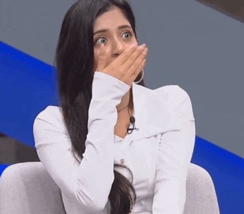 a woman in a white shirt is covering her mouth with her hands