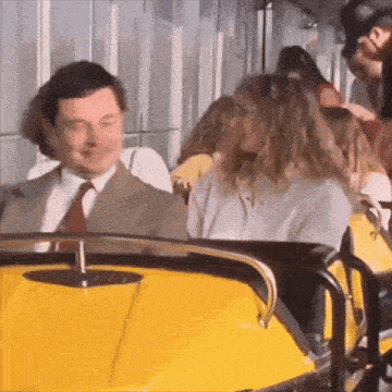 a man in a suit and tie is riding a roller coaster with a woman behind him