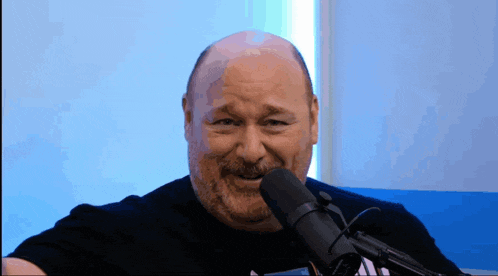 a bald man with a beard is sitting in front of a microphone and smiling