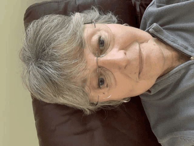 a woman wearing glasses and a grey shirt is laying down