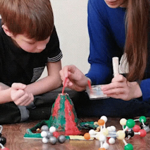 a boy and a girl are playing with a model of a volcano on the floor