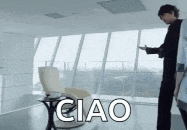 a man in a black suit stands in front of a large window with the word ciao above him