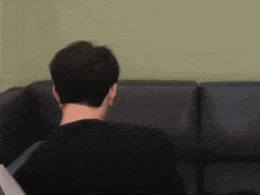 a man in a black shirt is sitting on a couch looking at something .