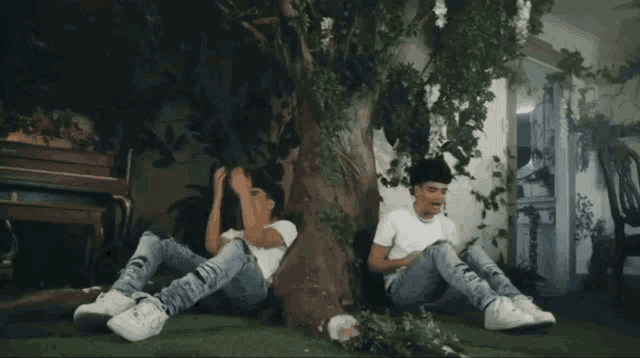 two young men are sitting under a tree talking to each other
