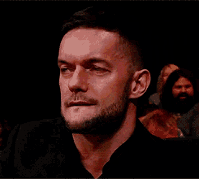 a man with a beard is sitting in a dark room and looking at the camera .
