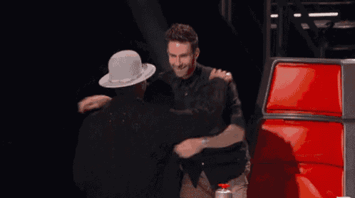 two men hugging each other in front of a red chair