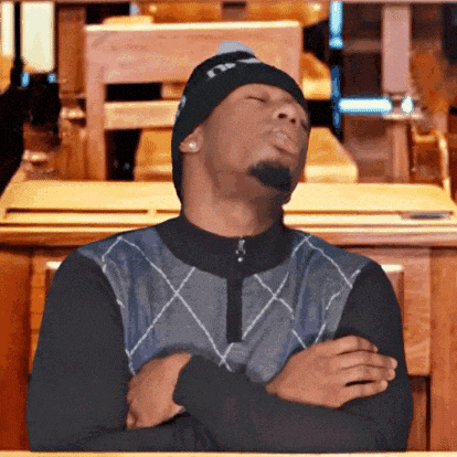 a man wearing a beanie and sweater is sitting at a table with his eyes closed .