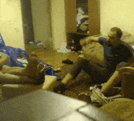 a man in a blue shirt is sitting on the floor with his feet up