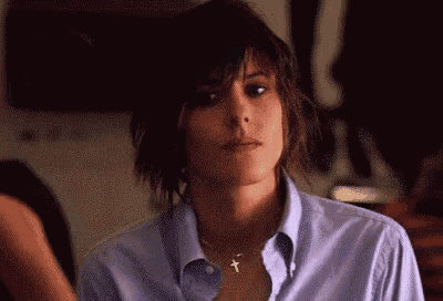 a woman wearing a purple shirt and a cross necklace is looking at the camera .