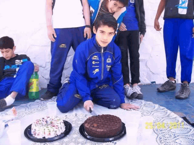 a boy wearing a blue jacket with pepsi written on it is cutting a cake