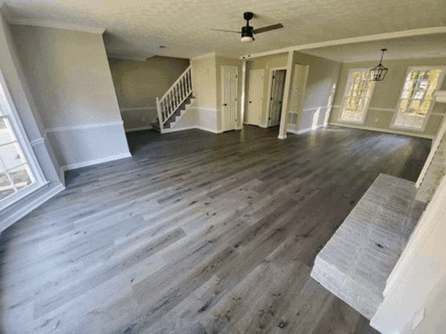 an empty living room with a ceiling fan and stairs