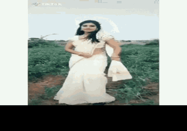 a woman in a white saree is standing in a field holding a towel .