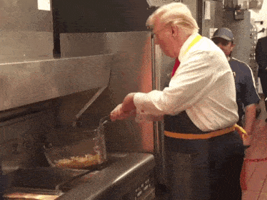 a man in an apron is cooking french fries in a kitchen