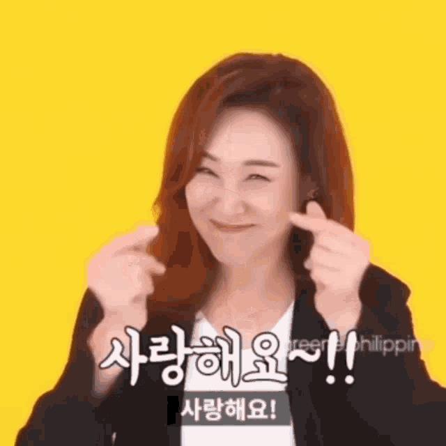a woman with red hair is smiling and making a heart shape with her fingers .