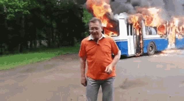 a man is standing in front of a burning bus on a road .