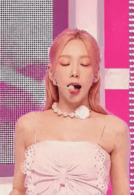 a close up of a woman wearing a pink dress and a pearl necklace with her tongue out .