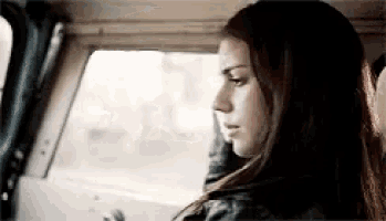 a woman is sitting in the driver 's seat of a car looking out the window .