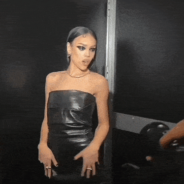 a woman in a black leather strapless dress stands in front of a black door