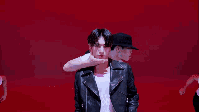 a man in a black leather jacket is standing in front of two other men wearing hats and white shirts .