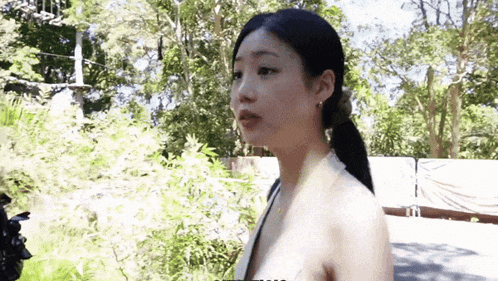 a woman in a white tank top is standing in front of a forest .