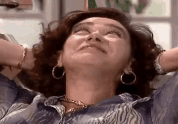 a woman wearing hoop earrings is sitting on a couch with her hands behind her head .