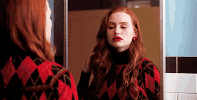 a woman with red hair is looking at herself in a bathroom mirror