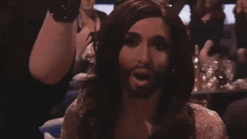 a man with a beard is surrounded by people applauding and laughing