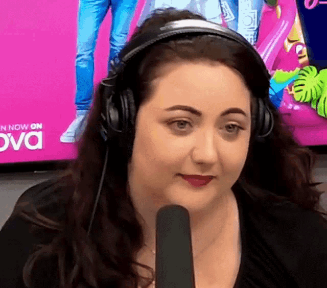 a woman wearing headphones is talking into a microphone in front of a tv screen that says now on