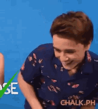 a man in a blue shirt is laughing in front of a blue background with the word chalk.ph on it .