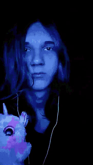 a young man with long hair holds a stuffed animal with a unicorn horn