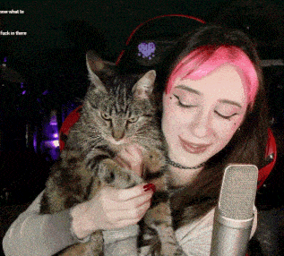 a woman holding a cat in front of a microphone with the words now what to fuck in there above her