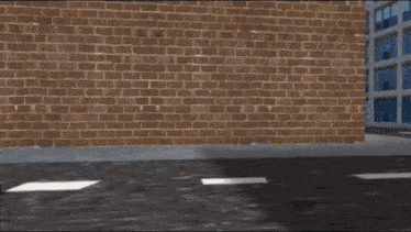 a red car is driving down a street in front of a building that has the letter r on it