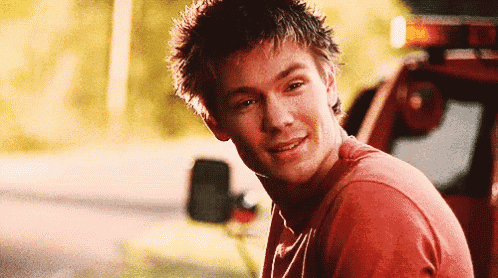 a young man in a red shirt is smiling while sitting in front of a truck .